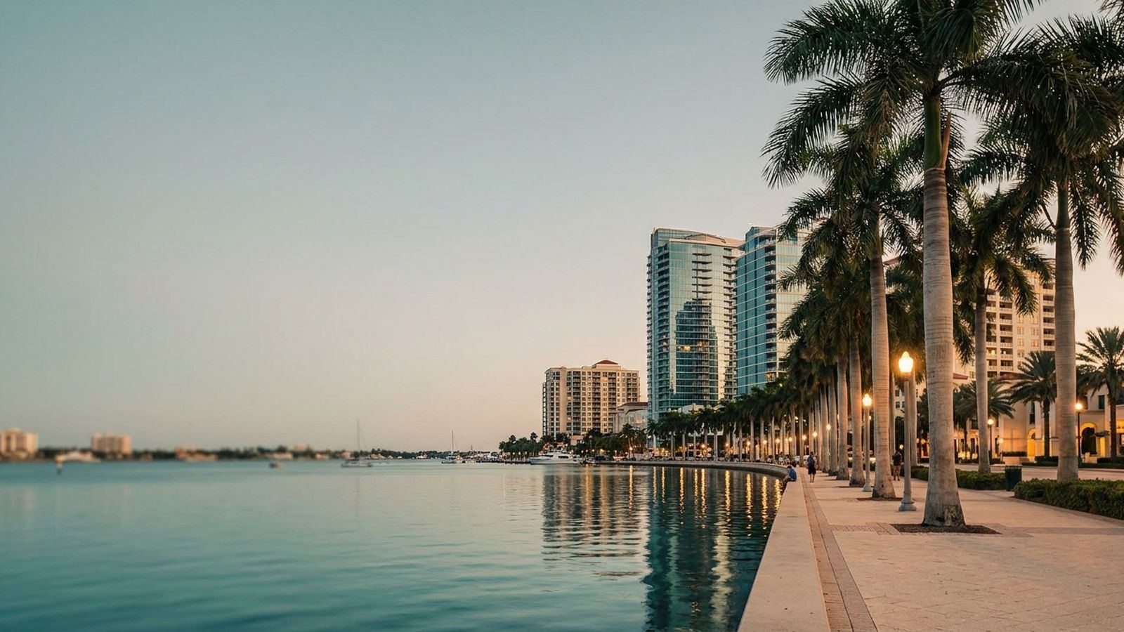 The downtown West Palm Beach waterfront at dusk with towers reflected in the Intracoastal and royal palms along the promenade